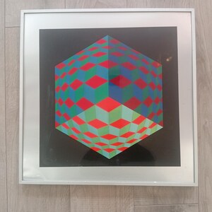 May include: A framed geometric art print featuring a three-dimensional cube design. The cube is composed of red, green, and blue diamond shapes against a black background. The artwork is encased in a silver frame, suitable for wall decor.