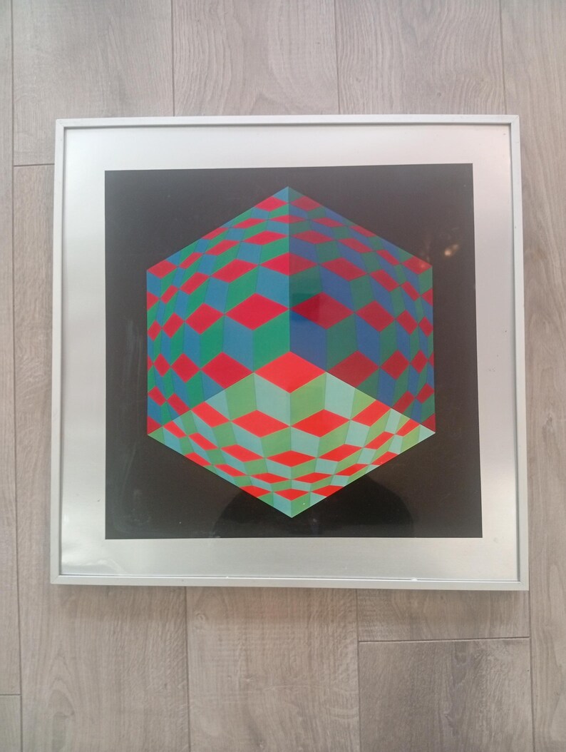 May include: A framed geometric art print featuring a three-dimensional cube design. The cube is composed of red, green, and blue diamond shapes against a black background. The artwork is encased in a silver frame, suitable for wall decor.