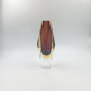 Peut inclure: Un vase en verre transparent au design géométrique. Le vase a un intérieur bordeaux foncé et un extérieur doré et transparent. Le vase est de forme haute et élancée avec une base rectangulaire.