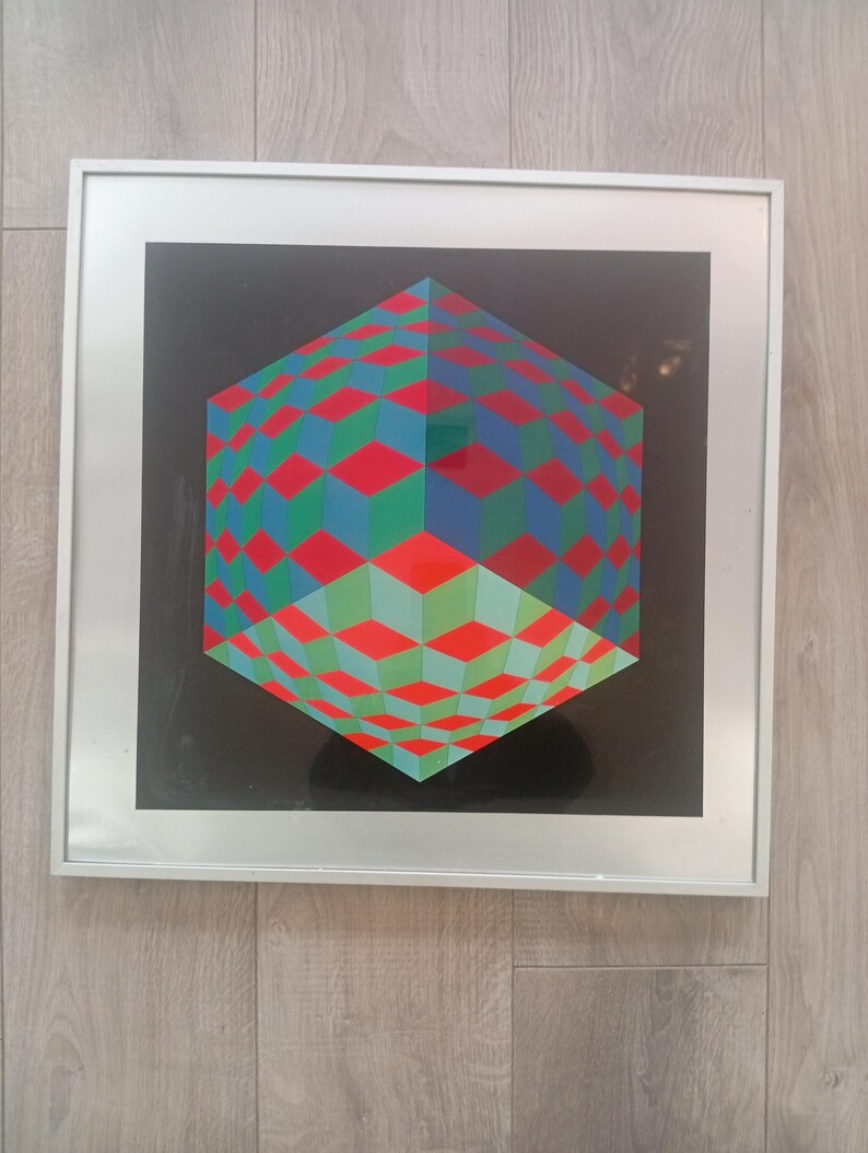 May include: Framed geometric art print featuring a 3D cube design. The cube is composed of red, green, and blue diamond shapes against a black background. The artwork is encased in a silver frame, creating a modern aesthetic.