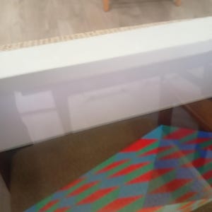 May include: A colorful geometric pattern in red, green, and blue, displayed within a glass-topped display case. The pattern features a repeating diamond design. The case is set against a neutral background.