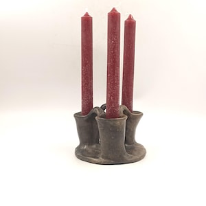 May include: A brown ceramic candle holder with three candle cups, holding three red candles.