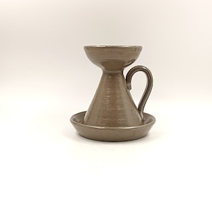 May include: A brown ceramic candle holder with a handle and a saucer base.