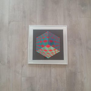 May include: Framed geometric art print featuring a 3D cube design. The cube is composed of red, green, and blue diamond shapes against a black background. The artwork is encased in a white frame.