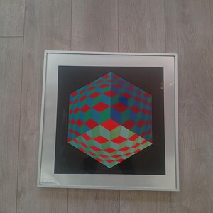 May include: A framed geometric art print featuring a three-dimensional cube design. The cube is composed of red, green, and blue squares against a black background. The artwork is encased in a silver frame.