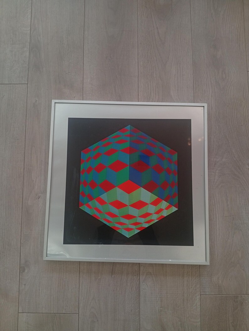 May include: A framed geometric art print featuring a three-dimensional cube design. The cube is composed of red, green, and blue squares against a black background. The artwork is encased in a silver frame.