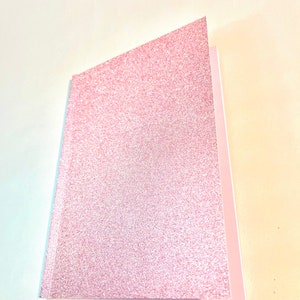 May include: A pink glitter notebook with a white spine.