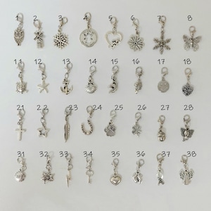 Pode incluir: Uma coleção de trinta e dois berloques de metal prateado, cada um com um fecho lagosta. Os berloques incluem formas como uma coruja, moinho, floco de neve, anjo, coração, flor, borboleta, tartaruga, estrela do mar, âncora, concha, golfinho, rosto sorridente, cruz, estrela, pena, ferradura, pata, trevo, elefante, raio, chave e fita.