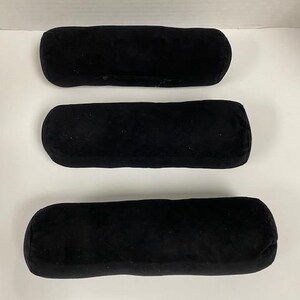 May include: Three black, cylindrical velvet display pillows. The pillows are arranged horizontally, with rounded ends and a soft, plush texture. They are designed to showcase jewelry or other small items.