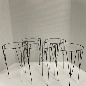 May include: A set of four dark metal plant supports, each featuring a circular top ring connected to multiple vertical wire legs that taper downward to form a sturdy structure for garden plants to grow upright in a container or soil.