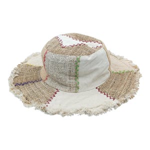 Könnte beinhalten: Ein Patchwork-Eimerhut mit ausgefranstem Rand. Der Hut hat eine Mischung aus beigen, weißen und hellbraunen Stoffen mit Akzenten aus roten, grünen und violetten Nähten. Der Hut ist für Sonnenschutz und Freizeitkleidung konzipiert.