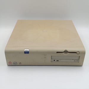 May include: A beige Dell OptiPlex GX1 desktop computer case with a flat, rectangular design. The front panel features a disk drive slot, a power button, indicator lights, and small Dell, Intel, and Windows logos in the bottom left corner.