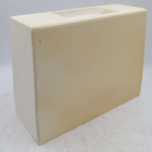 May include: A rectangular, off-white plastic carrying case with a smooth, solid surface and a recessed handle opening at the top. The case features rounded vertical edges and shows minor surface scuffs and discolouration on the exterior shell.