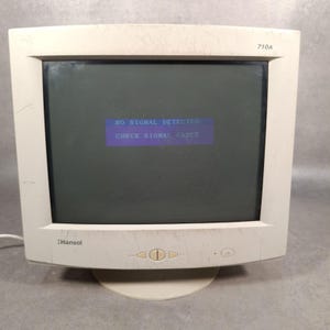 May include: Off-white Hansol computer monitor with a dark screen displaying the message "NO SIGNAL DETECTED. CHECK SIGNAL CABLE." The monitor has a rounded base and a few buttons on the front.