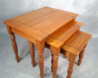 May include: Set of three wooden nesting tables. The tables are made of light brown wood with a rectangular top and turned legs. The largest table is approximately 24 inches wide, 16 inches deep, and 20 inches tall.