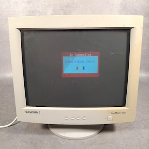 May include: A cream-coloured Samsung SyncMaster 753s computer monitor displays a "No Connection" message with "Check Signal Cable" text. The screen shows a red rectangle with a blue rectangle and three coloured bars. The monitor has a white base and a power button.