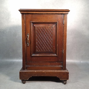 May include: An antique wooden cabinet, featuring a single door with a diamond-patterned central panel. It has a brass handle and sits on small wheels. The dark brown wood finish indicates age and quality. The cabinet's height is approximately 76 cm.