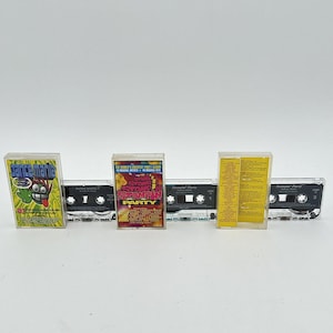 May include: Five vintage cassette tapes are displayed. The tapes have colourful album art with text and graphics. The cassette cases are clear plastic, and the tapes are black. The album art includes the words "Dancemania" and "Stomp Stompin' Party."
