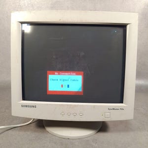 May include: A white Samsung SyncMaster 753s computer monitor. The dark screen displays a red box with the text "No Connection" and "Check Signal Cable". The monitor has a round base and several buttons.