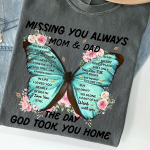 May include: A gray t-shirt with a butterfly graphic and the text "Missing You Always Mom & Dad The Day God Took You Home". The butterfly is blue and green with pink flowers around it. The text is in black.
