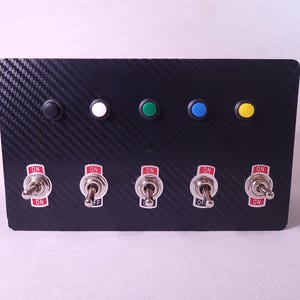 May include: A black panel with five round buttons in black, white, green, blue, and yellow. Below the buttons are five toggle switches with red "ON" and "OFF" labels.
