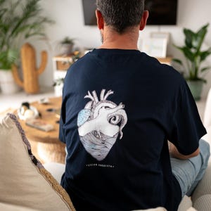 Könnte beinhalten: Marineblaues T-Shirt mit detailliertem anatomischem Herzdesign und Meereswellen, mit dem Text "Lilian Urquieta." Die Grafik ist in Weiß und Hellblau gehalten. Das Shirt besteht aus einem weichen Material.