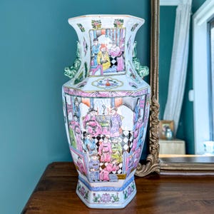 May include: An elaborate porcelain vase with a multi-faceted design. The vase is adorned with hand-painted scenes in pink, blue, yellow, and green, showing figures in a traditional setting. It has green dragon-shaped handles and floral patterns.