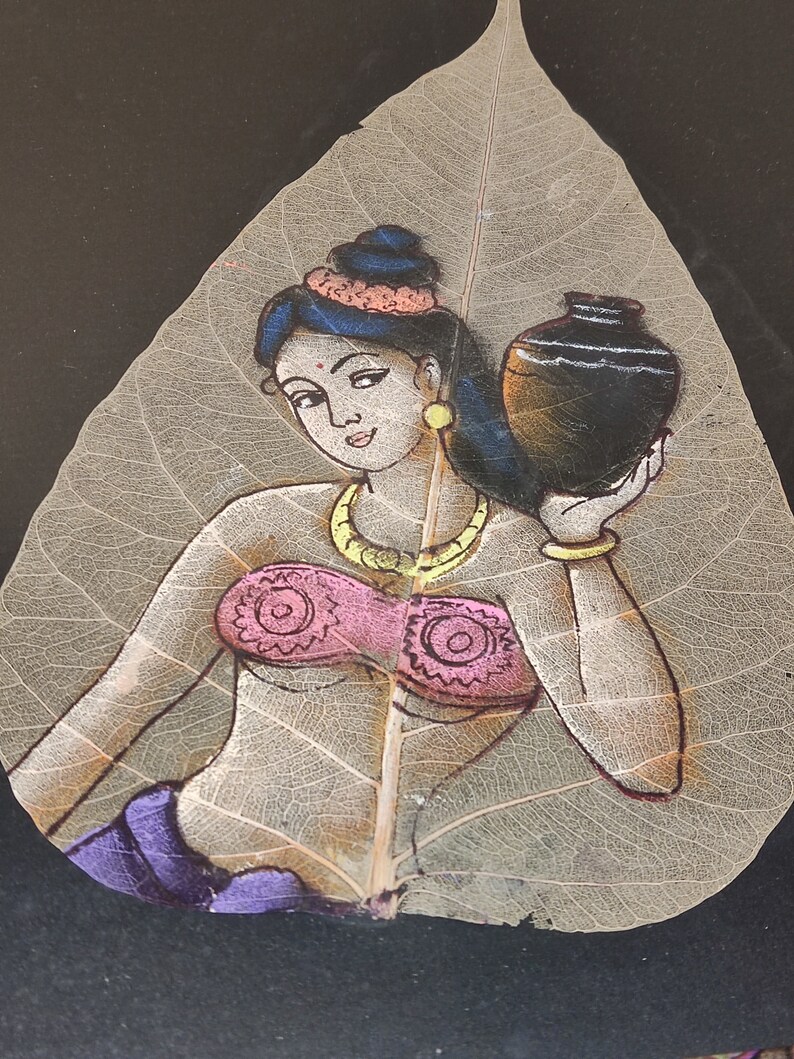 May include: A painting of a woman holding a pot, painted on a dried leaf. The woman is wearing a pink top, a purple skirt, and a gold necklace. The leaf is light brown and has a delicate vein pattern.