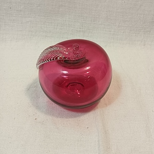 May include: A red glass apple with a clear glass stem and leaf. The apple is a decorative object.