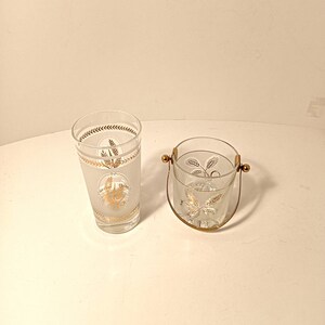 May include: Two vintage clear glass barware items with gold leaf patterns. One is a tall glass, the other an ice bucket with a gold handle. Both have a frosted finish and gold accents, ideal for serving drinks.