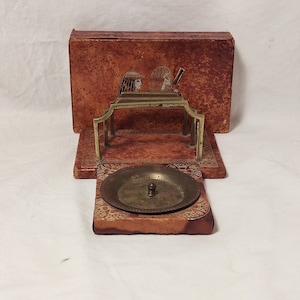 May include: A vintage brass and leather ashtray with an Egyptian design. The ashtray has a round dish with a small knob in the centre and a stand with two vertical supports. The leather is brown with a textured surface and the stand has a decorative design.