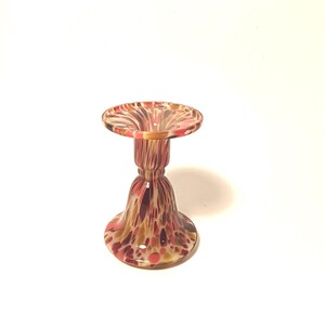 May include: A decorative glass candle holder with a flared base and a wide, shallow top. The glass is speckled with red, brown, and yellow hues. The candle holder is approximately 13 cm tall.