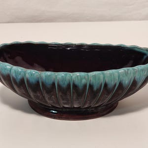 Könnte beinhalten: Ovale Keramik-Blumenschale mit dunkelbraunem Innenraum und türkisfarbenem Rand. Das Äußere hat ein geripptes Design, und die Schale steht auf einem passenden braunen Sockel. Geeignet für Zimmerpflanzen.
