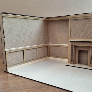 May include: A miniature room model with a fireplace and wood paneling. The walls are painted a light beige color and the trim is white. The floor is a light brown color.