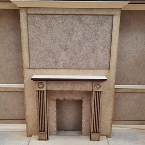 May include: A beige wooden fireplace mantel with a black trim and a rectangular opening for a fire. The mantel is set against a beige wall.