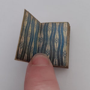 May include: A small, closed book with a blue and cream patterned cover. The book is open to reveal the inside pages.