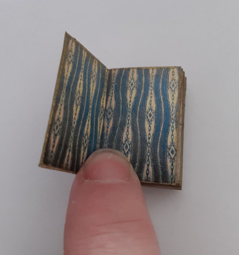 May include: A small, closed book with a blue and cream patterned cover. The book is open to reveal the inside pages.