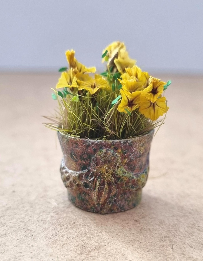 Pode incluir: Um pequeno vaso de flores cheio de flores amarelas e grama verde. O vaso &eacute; uma mistura de cores marrom, verde e dourado com uma superf&iacute;cie texturizada. As flores t&ecirc;m centros vermelho escuro.