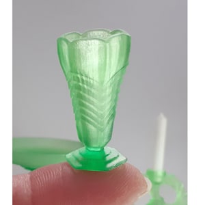 May include: A small, green glass vase with a fluted design. The vase has a wide mouth and a narrow base.