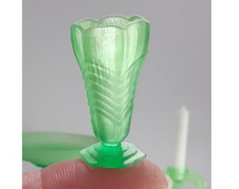 May include: A small, green glass vase with a fluted design. The vase has a wide mouth and a narrow base.