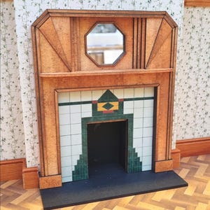 Peut inclure: Cheminée miniature en bois avec un miroir octogonal, présentant un design géométrique. La cheminée a un intérieur sombre et est décorée de carreaux verts, blancs et orange. Le manteau est de couleur marron clair.