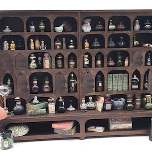 May include: A miniature wooden apothecary cabinet, stained dark brown, filled with tiny glass bottles, jars, and books. The cabinet has multiple shelves. A hand is visible in the foreground.