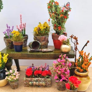 Pode incluir: Cena de jardim em miniatura com v&aacute;rias plantas e flores em vasos. Inclui um pequeno banco de madeira com uma esp&aacute;tula e um vaso virado. A cena apresenta uma variedade de flores coloridas, incluindo flores amarelas, rosas, vermelhas e laranjas, em vasos decorativos.