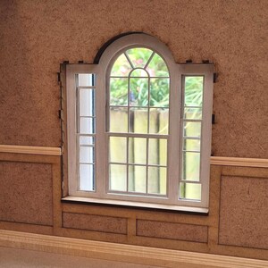May include: A white wooden window frame with a large arched window and two smaller rectangular windows on either side. The window is set into a brown wall with wood paneling.