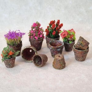 May include: A selection of miniature terracotta flower pots, some containing vibrant artificial flowers in purple, pink, red, and green. Several empty pots are also present, displaying a rustic, textured finish.