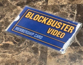 May include: A Blockbuster Video membership card in a clear plastic sleeve. The card has a blue background with the words "BLOCKBUSTER VIDEO" in yellow and "MEMBERSHIP CARD" in white.