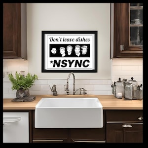 May include: A black and white framed print with the text "Don't leave dishes *NSYNC" and a row of five black and white images of men's faces. The print is hanging on a white tiled wall above a white farmhouse sink in a kitchen.