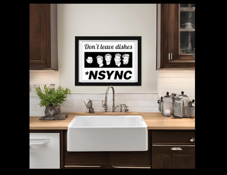 May include: A black and white framed print with the text "Don't leave dishes *NSYNC" and a row of five black and white images of men's faces. The print is hanging on a white tiled wall above a white farmhouse sink in a kitchen.