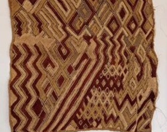 May include: A woven textile with a geometric pattern in shades of brown and tan. The design features zigzags, diamonds, and angular shapes. The textile appears to be handmade, with visible threads and a textured surface. The overall aesthetic is rustic and earthy.
