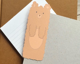 May include: A brown bear bookmark with a fuzzy texture and a simple face.